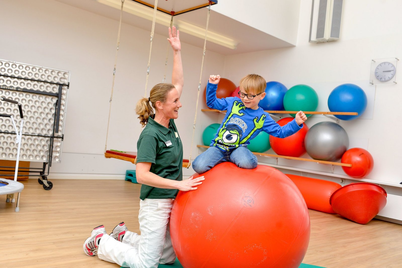 Kind auf einem Gymnastikball mit Therapeutin in der Ergotherapie 